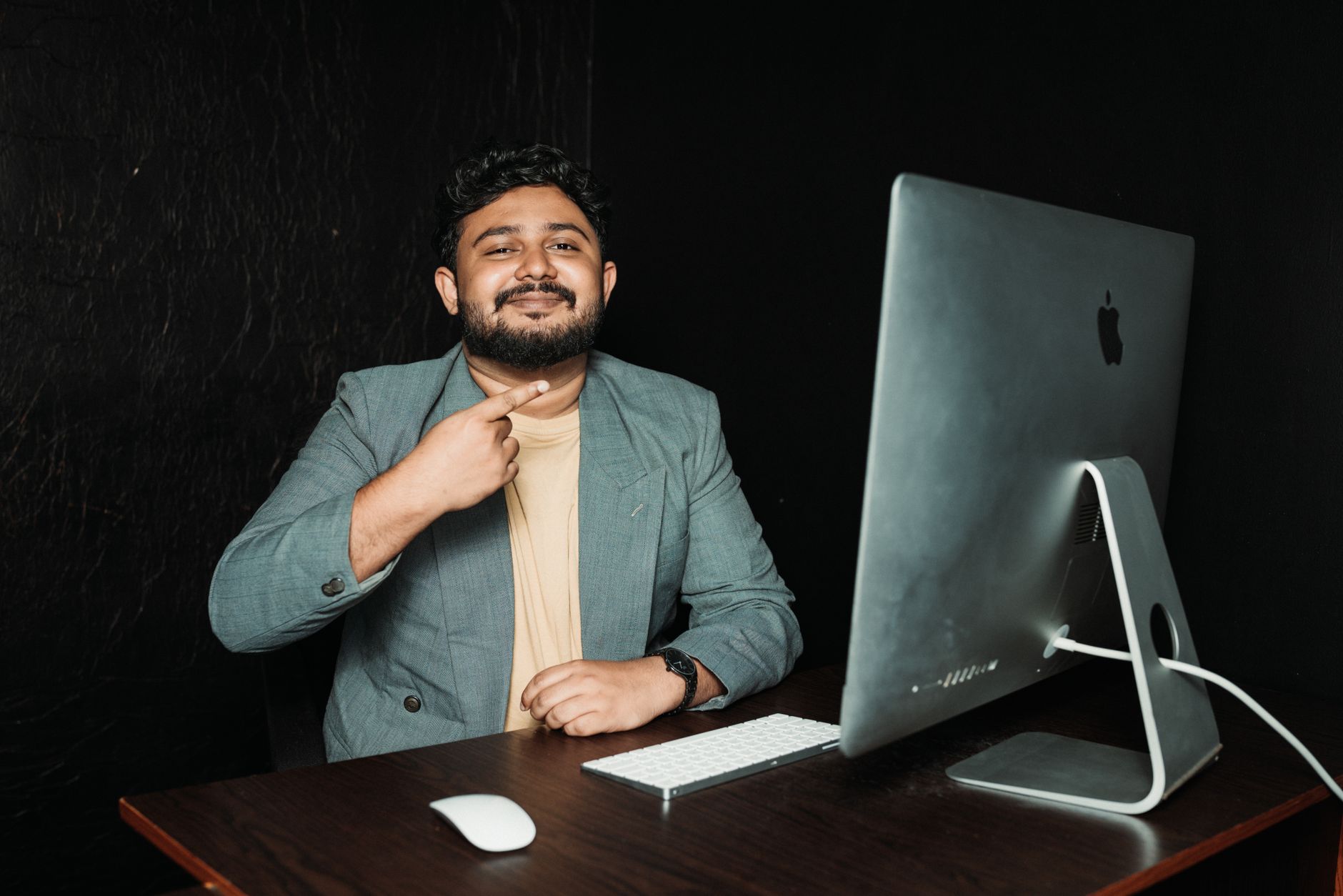 Man in a modern office setting, smiling at the camera with a desktop computer, showcasing professional tech environment